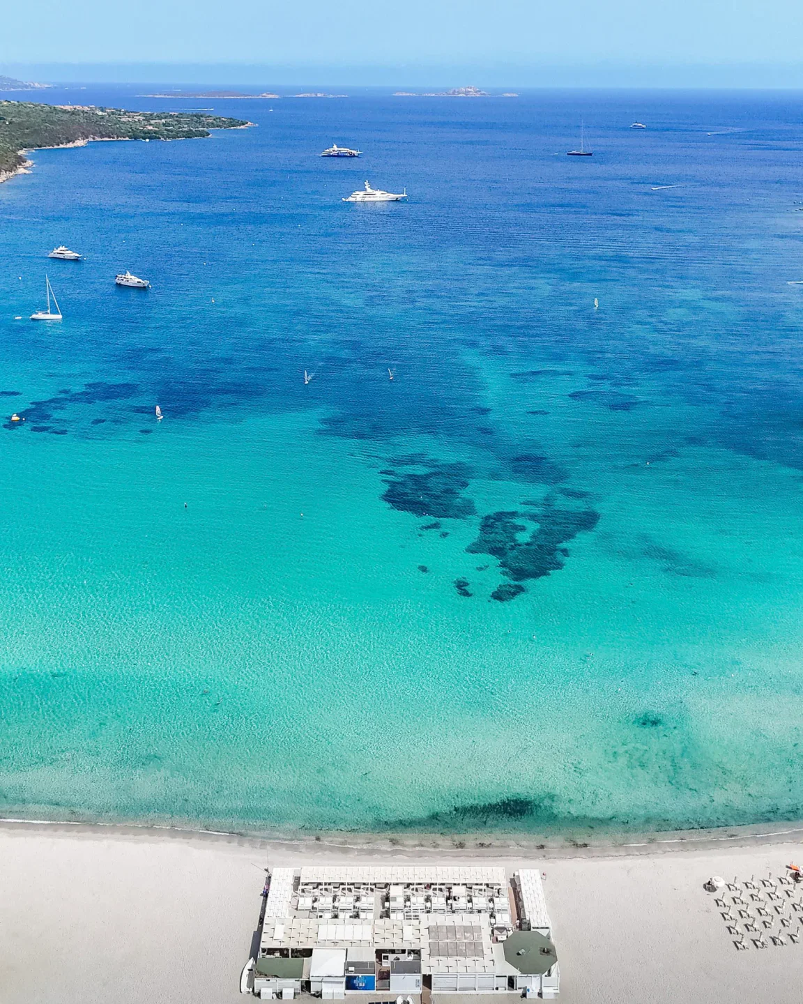 Blu Beach Sardinia: stunning aerial view of white sand beach with turquoise waters and yachts offshore.